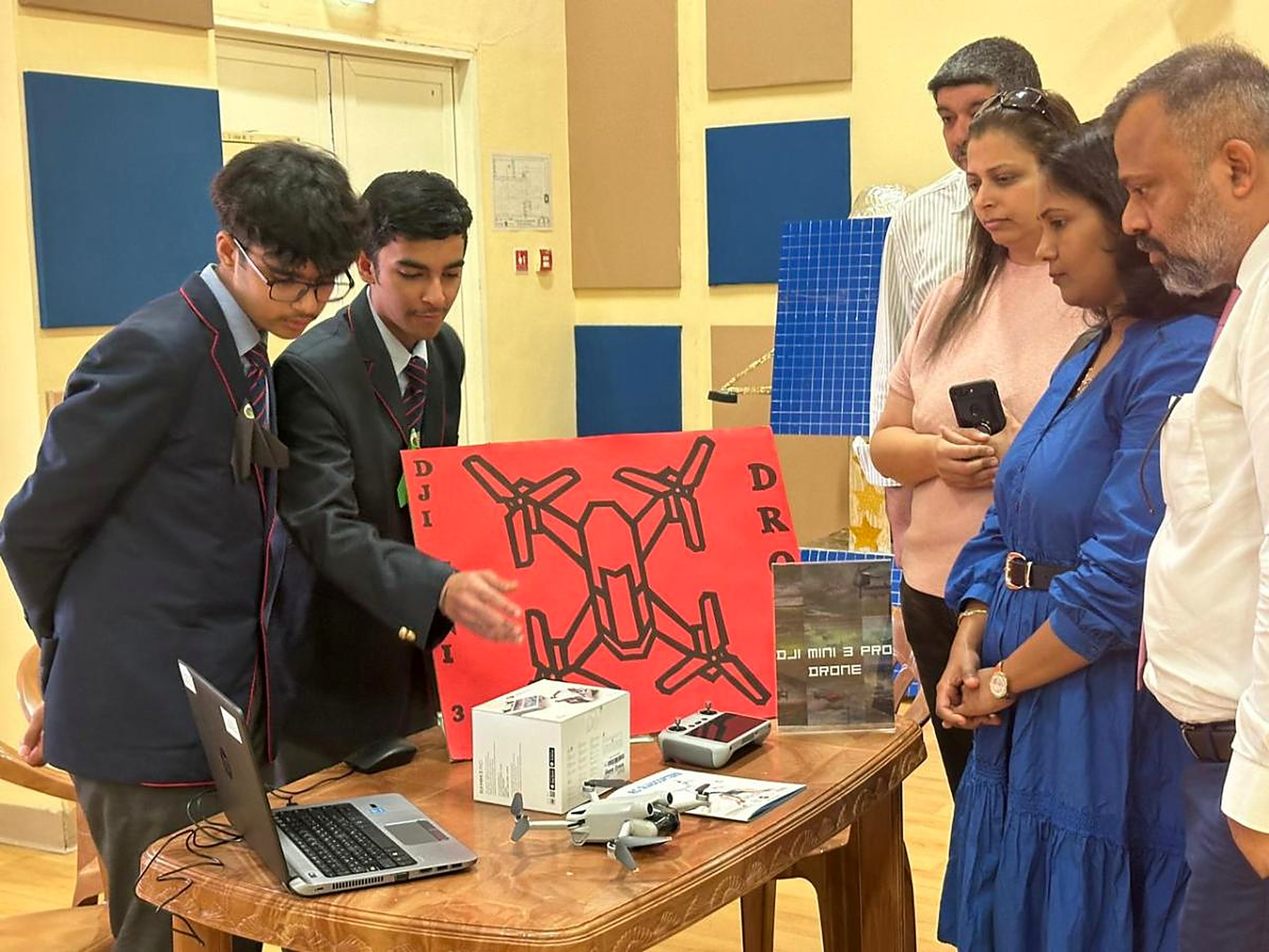 Two students demonstrating a DJI Mini 3 Pro drone and laptop flight software to parents at an MRS project showcase