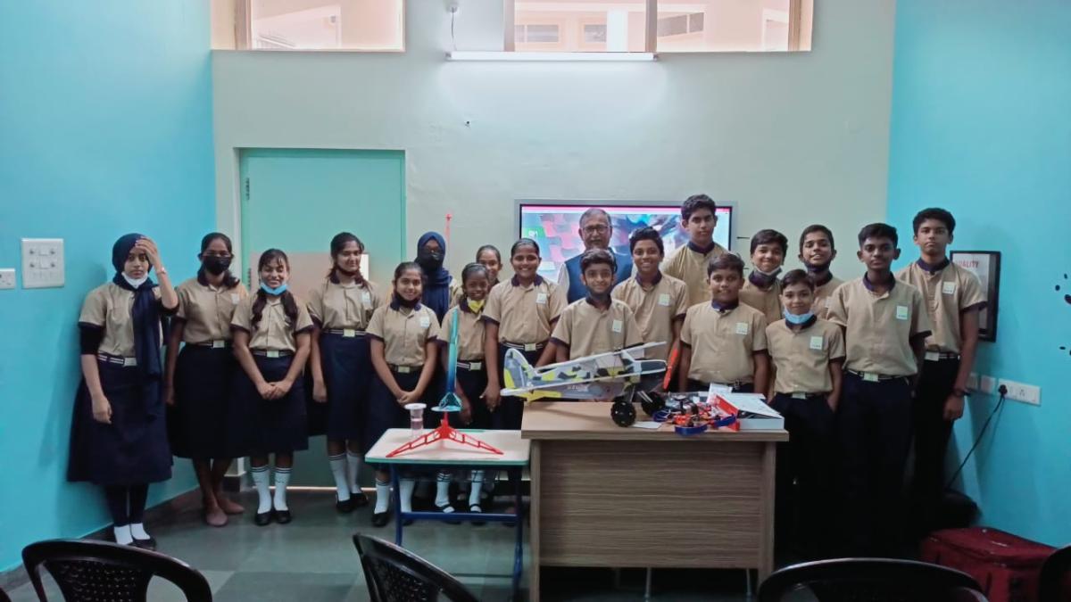 A school project team standing behind a table displaying a model aircraft, drone, water rocket launcher and small engineering builds