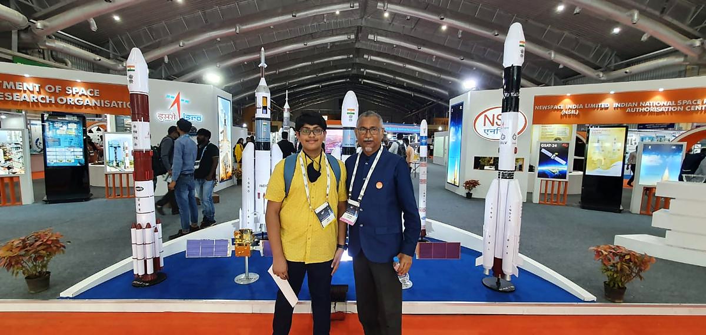 A student and mentor standing in front of full-size PSLV and GSLV launch vehicle models at an ISRO space exhibition hall