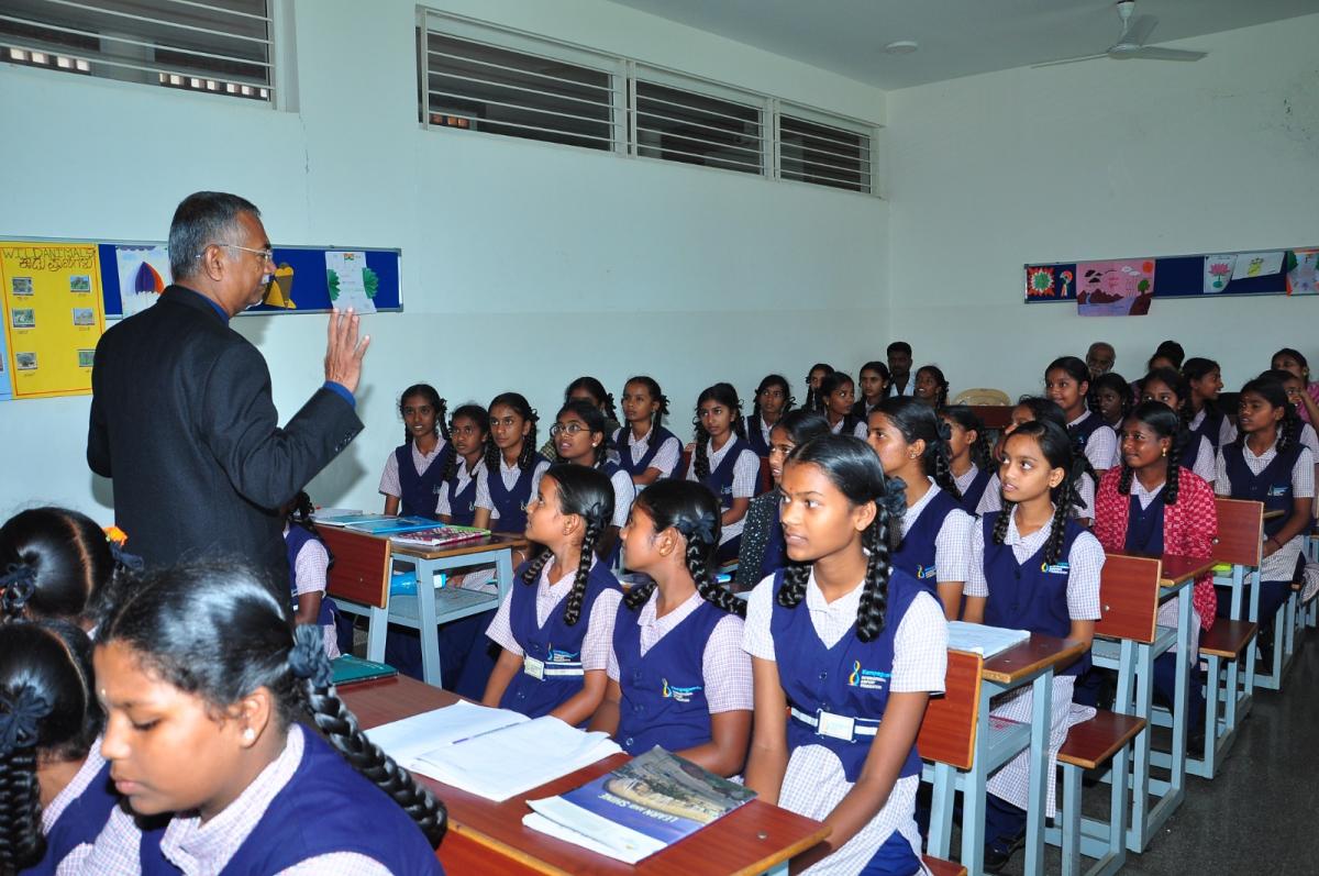 A mentor speaking to a full classroom of schoolgirls seated at their desks during an aerospace learning session
