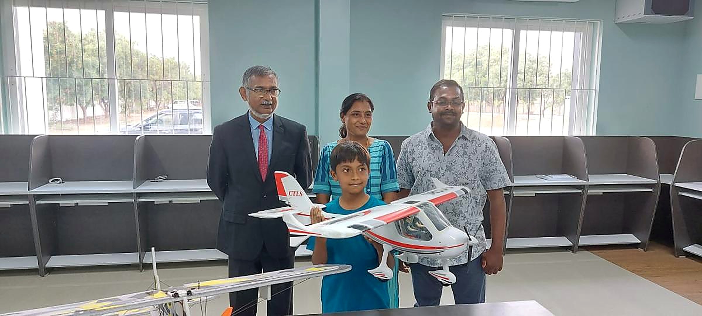 A mentor, two parents and a young student holding a large radio-controlled aircraft together in the aeromodelling lab