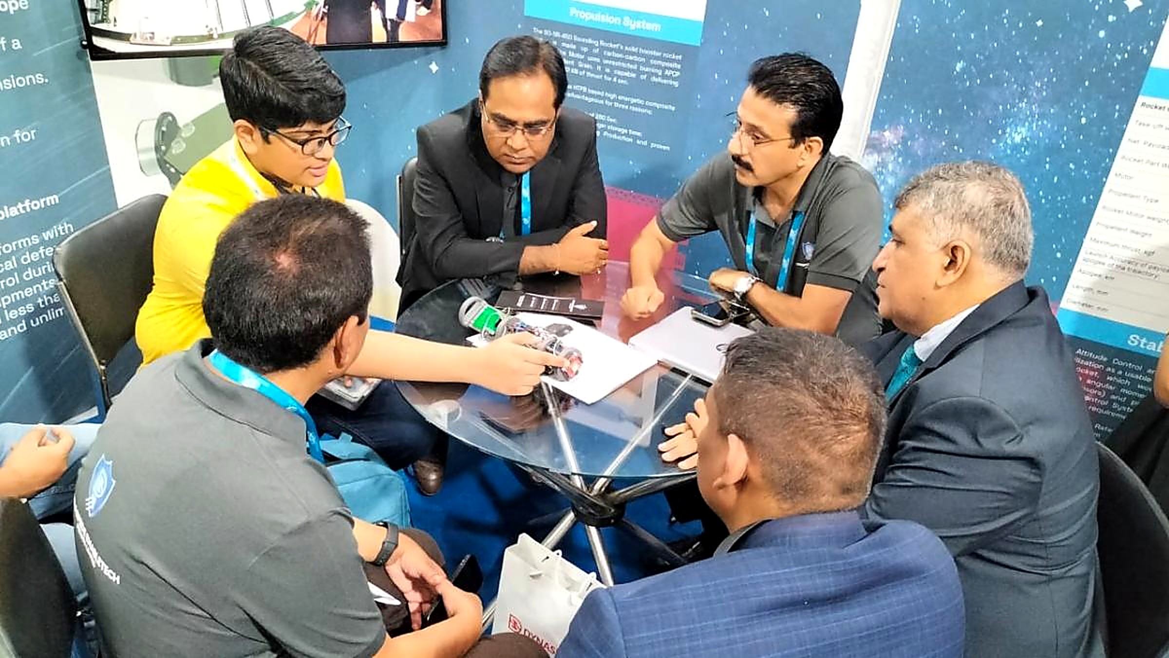 A student and several aerospace professionals in discussion around a glass table at a sounding rocket exhibition stand