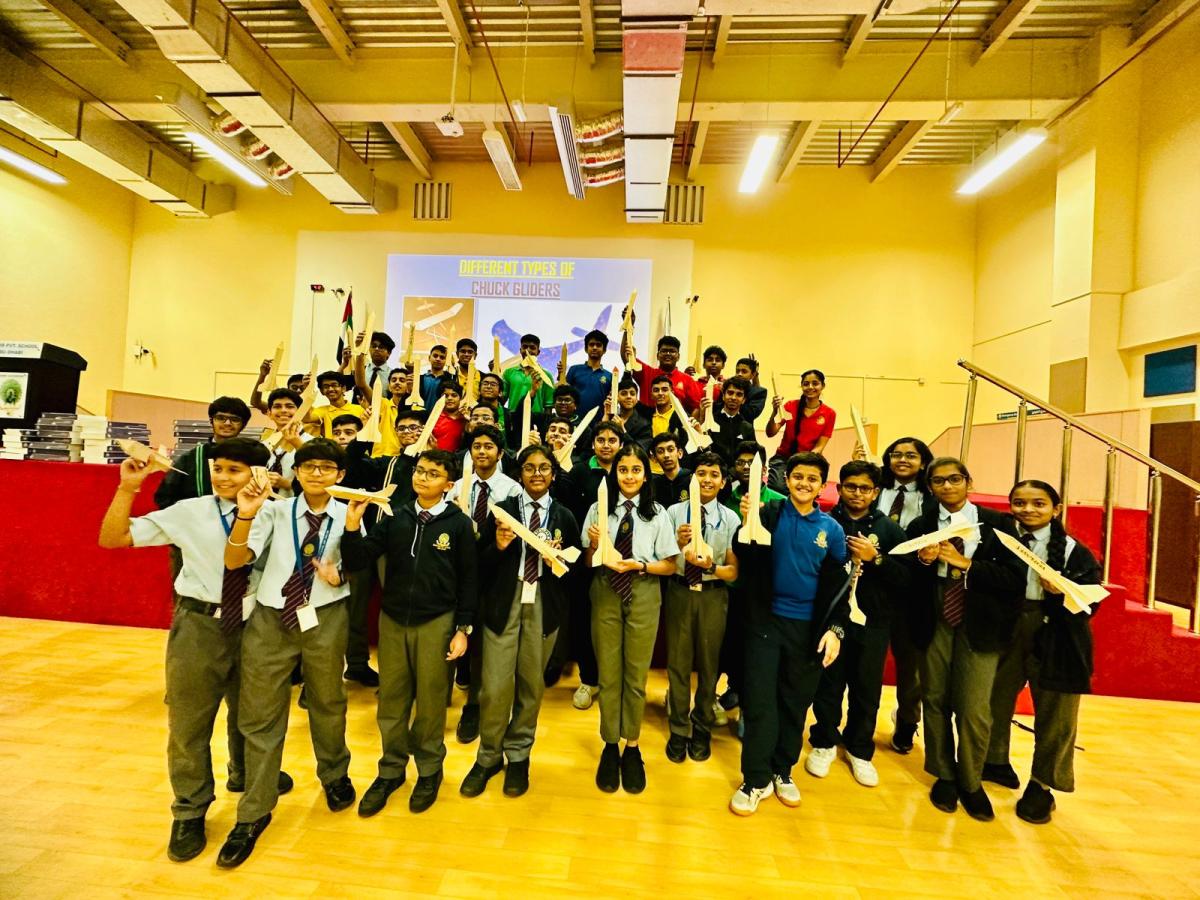 A large group of school students holding the chuck gliders they built during an MRS workshop in an auditorium