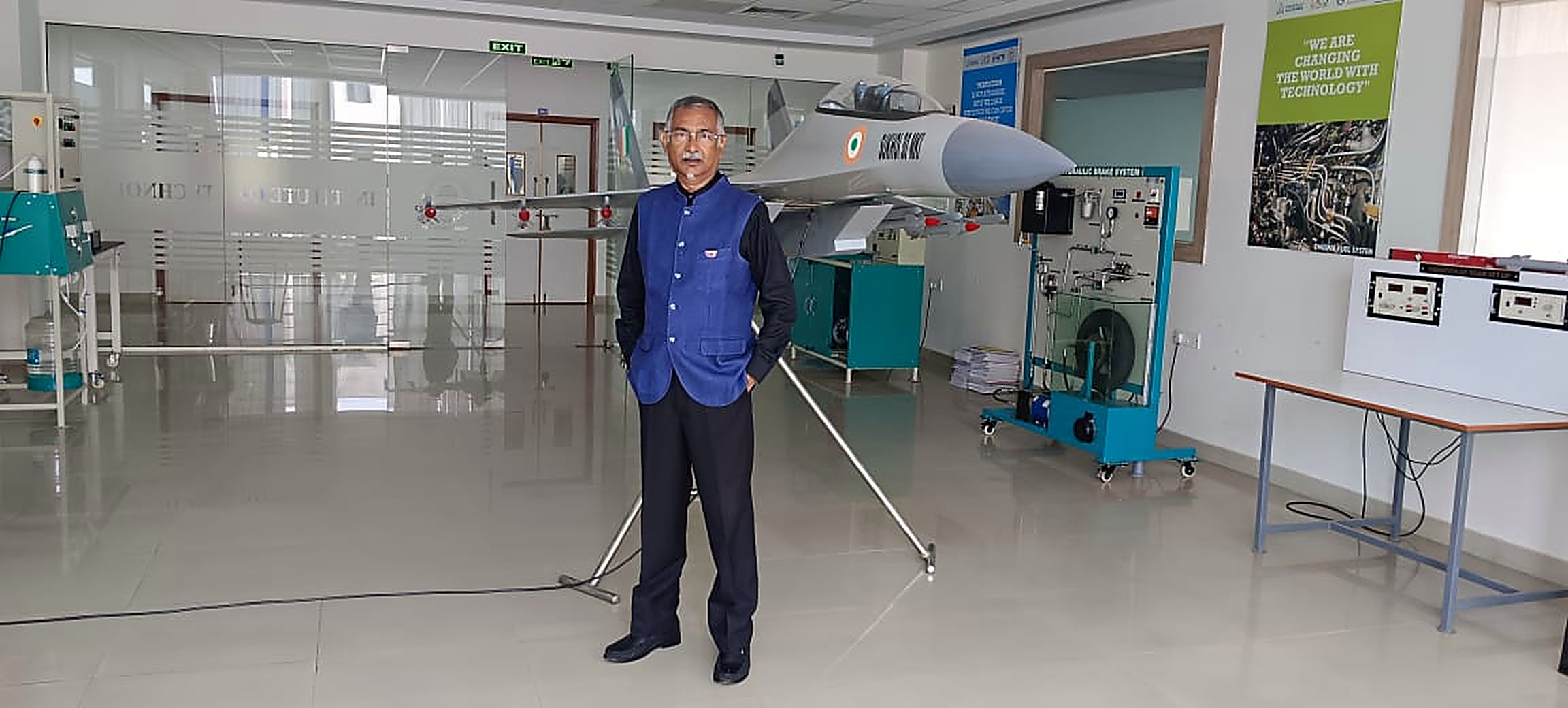 A mentor standing in an aerospace engineering lab in front of a full-size Tejas fighter aircraft model and test equipment
