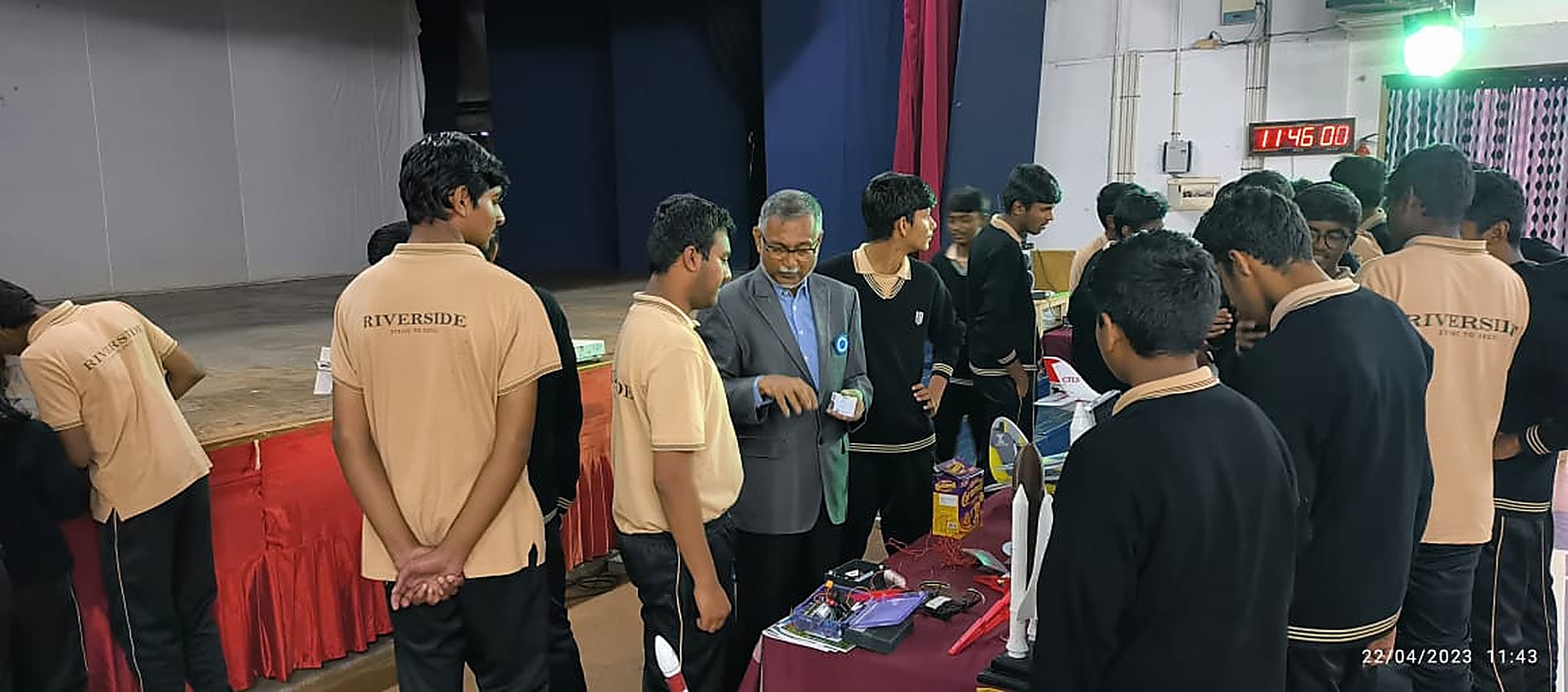 Students crowded around an exhibition table of rockets, electronics and RC aircraft in a school auditorium during an MRS showcase
